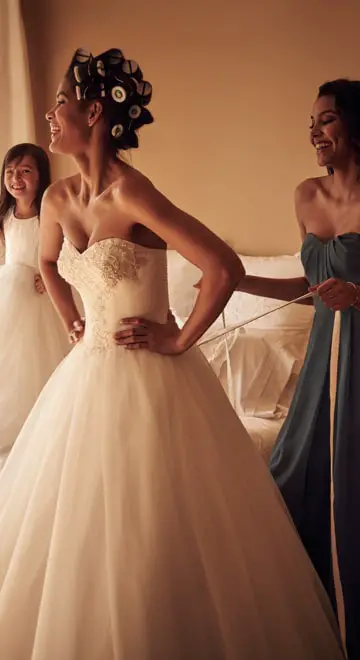 Woman wearing a gown smiling while other woman fixing her gown