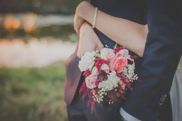 bride holding wedding bouquet while hugging the groom  